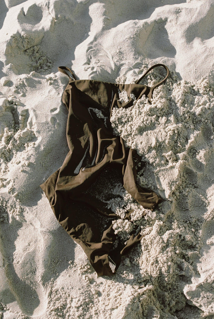 Black one-piece swimsuit partially covered in light sand on beach
