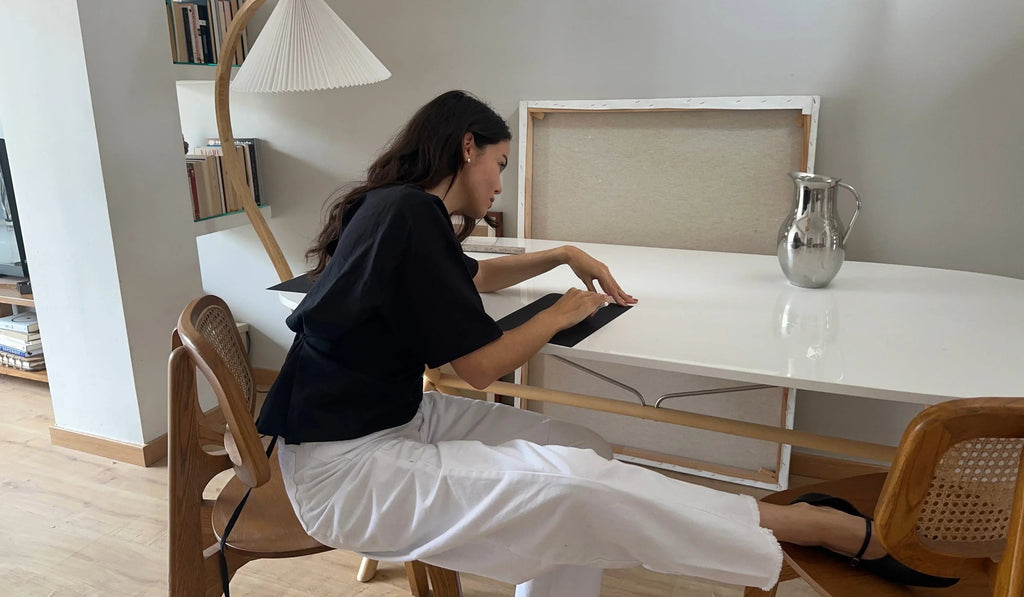 Woman folding black paper on a white desk in a modern room with wooden chairs and silver pitcher