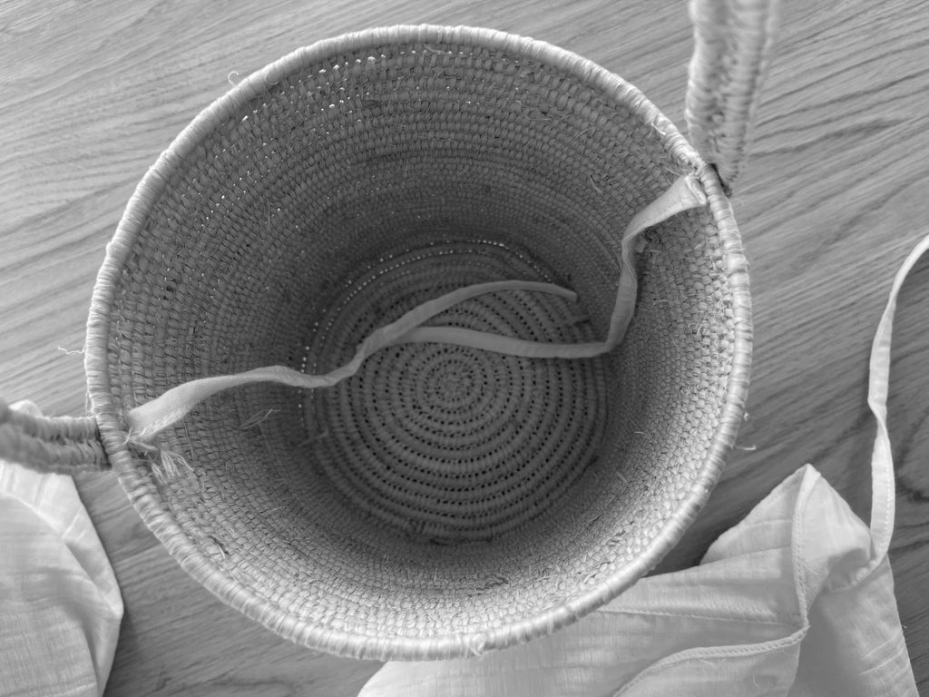 Top view of an empty woven straw basket with handles on a wooden floor with white fabric nearby