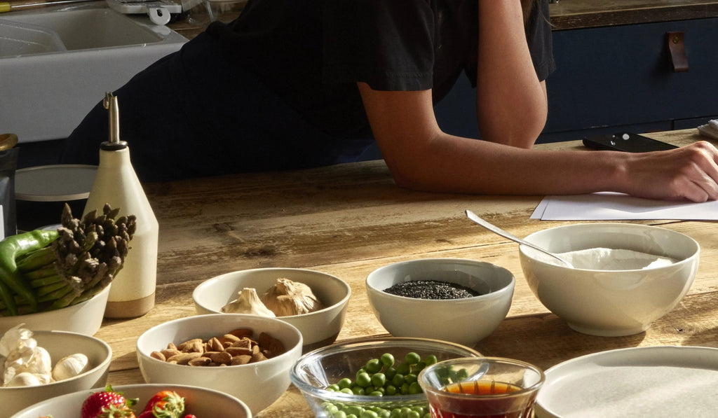Cooking ingredients including asparagus, garlic, almonds, seeds, sugar, peas, and honey on a wooden kitchen table