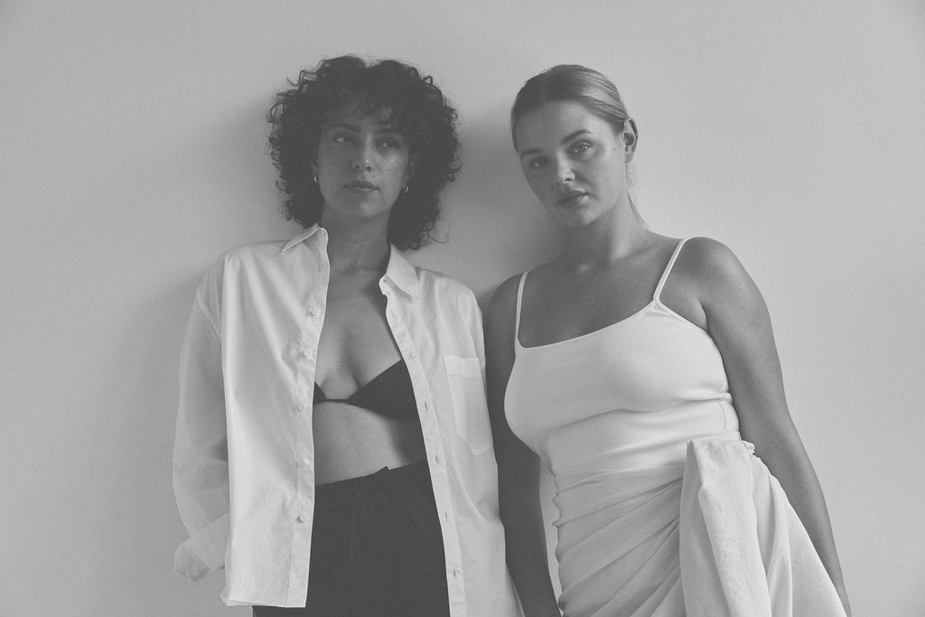 Black and white fashion portrait of two women in stylish minimalist outfits against plain white background