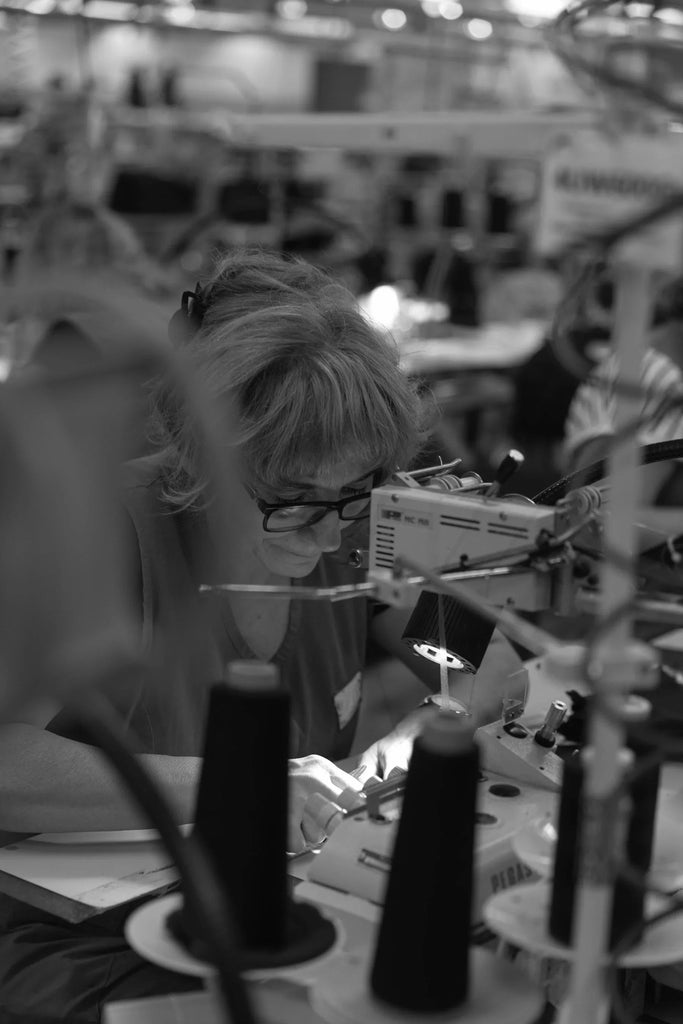 Woman sewing fabric intently at industrial sewing machine in garment factory with thread spools