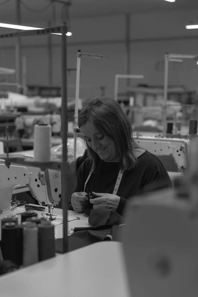 Woman sewing fabric with measuring tape in tailoring factory with sewing machines and threads