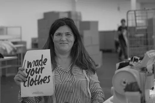 Woman in striped shirt holding sign saying I made your clothes in a textile factory with sewing machines