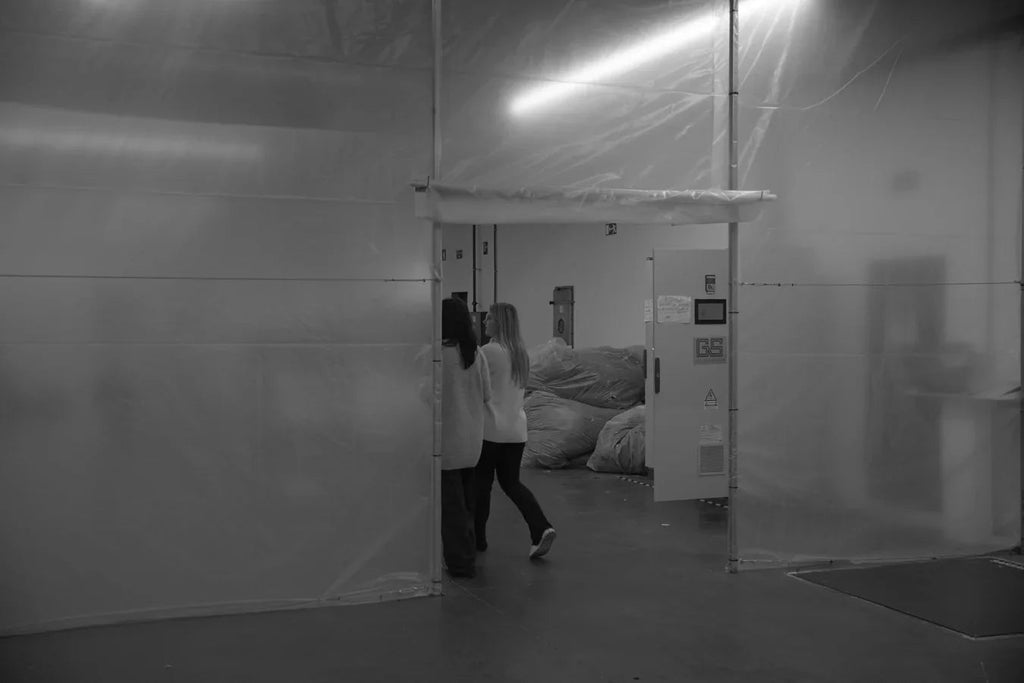 Two women walking inside a recycling factory with large plastic-covered piles and industrial equipment