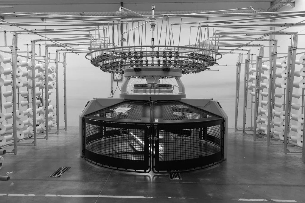 Industrial circular knitting machine in textile factory with yarn cones on racks