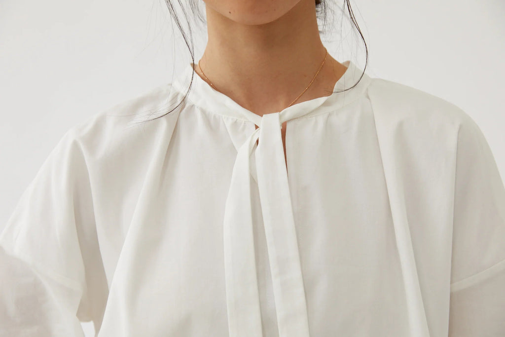 Close-up of a woman wearing a white blouse with a tie neckline and delicate gold necklace