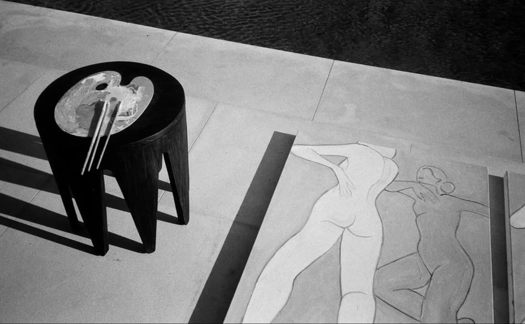 Black stool with artist palette and brushes beside abstract nude figure drawings on floor