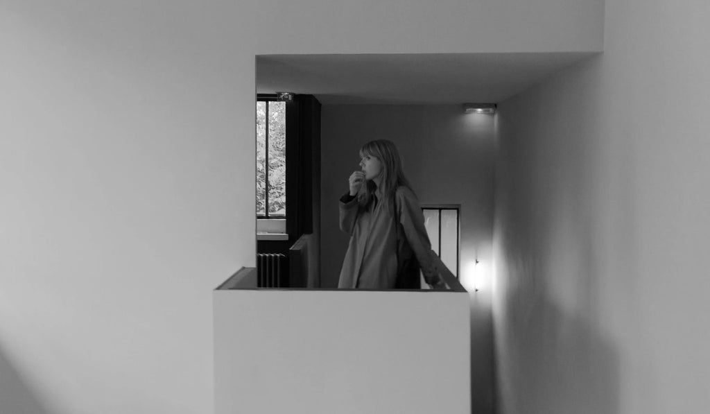 Black and white photo of a woman standing on an indoor balcony near window and wall lights