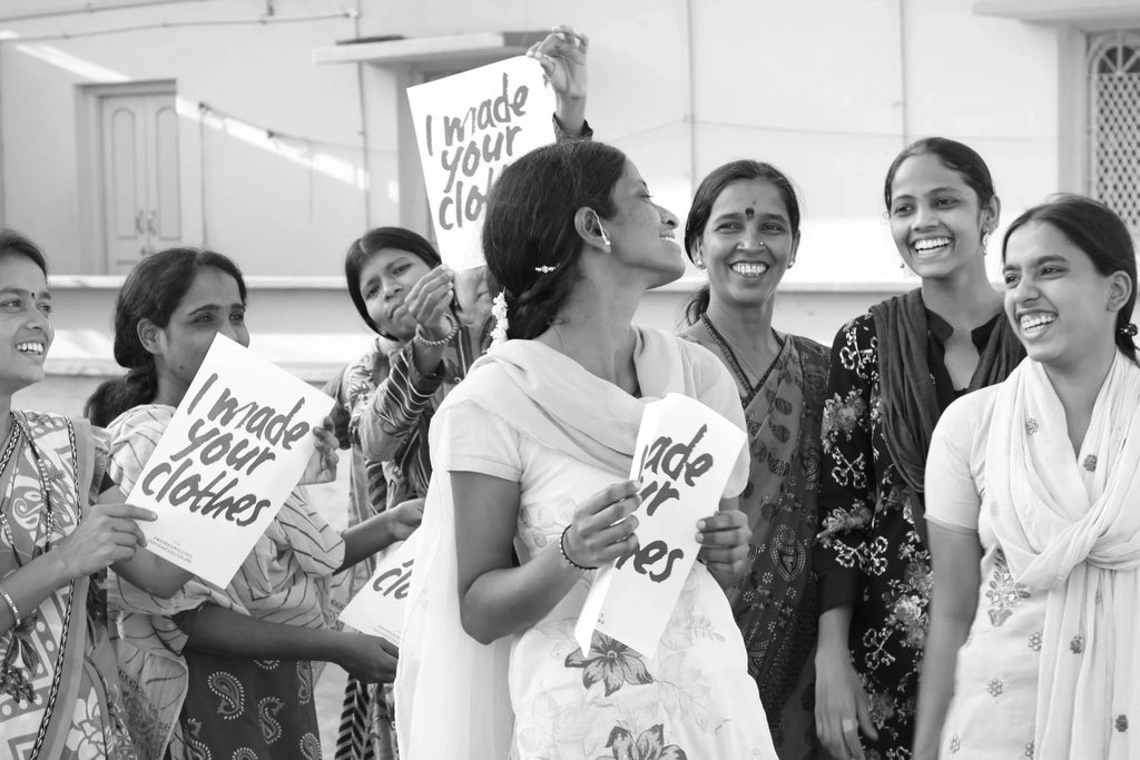 Group of smiling Indian women holding signs that say I made your clothes, promoting ethical clothing production