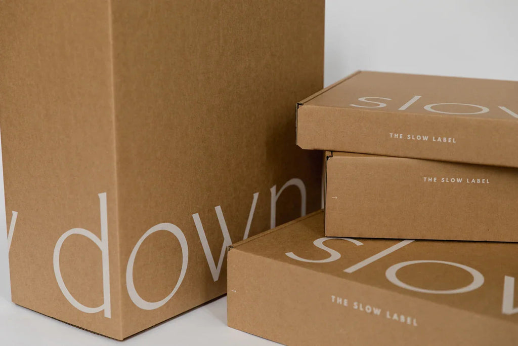 Minimalist brown cardboard boxes with The Slow Label branding and large white text on side